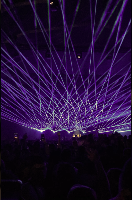 Exclusive corporate event in a physical venue infused with digital generative art, where giant screens show golden light waves built together by the team.